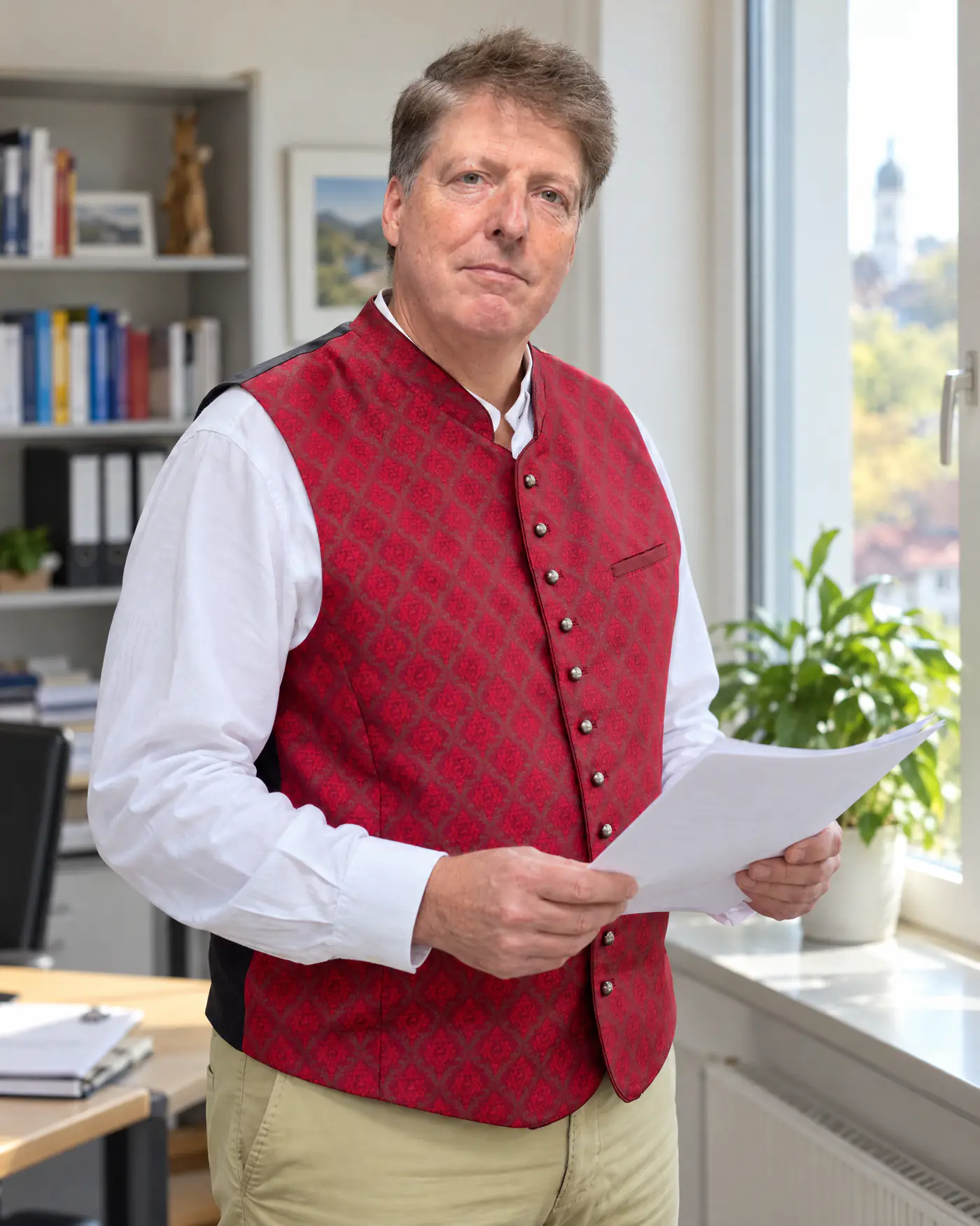 Alexander Solya in roter Trachtenweste liest in seinem Büro am Fenster ein Schriftstück, Bild mit KI erzeugt